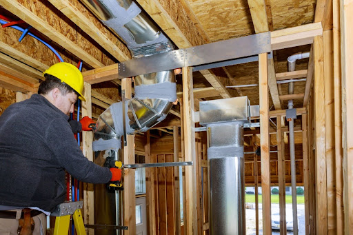 A man with a hard hat performing a service on ductwork in a home.